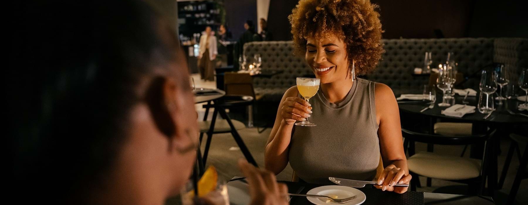 Two women sitting in a restaurant with one woman holding a glass drink and smiling.